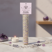 A tall clear plastic bag containing a bundle of dried blue sage and lavender smudge sticks, wrapped with purple lavender vines. The bundle has a hanging tag that reads  'BLUE SAGE & LAVENDER.