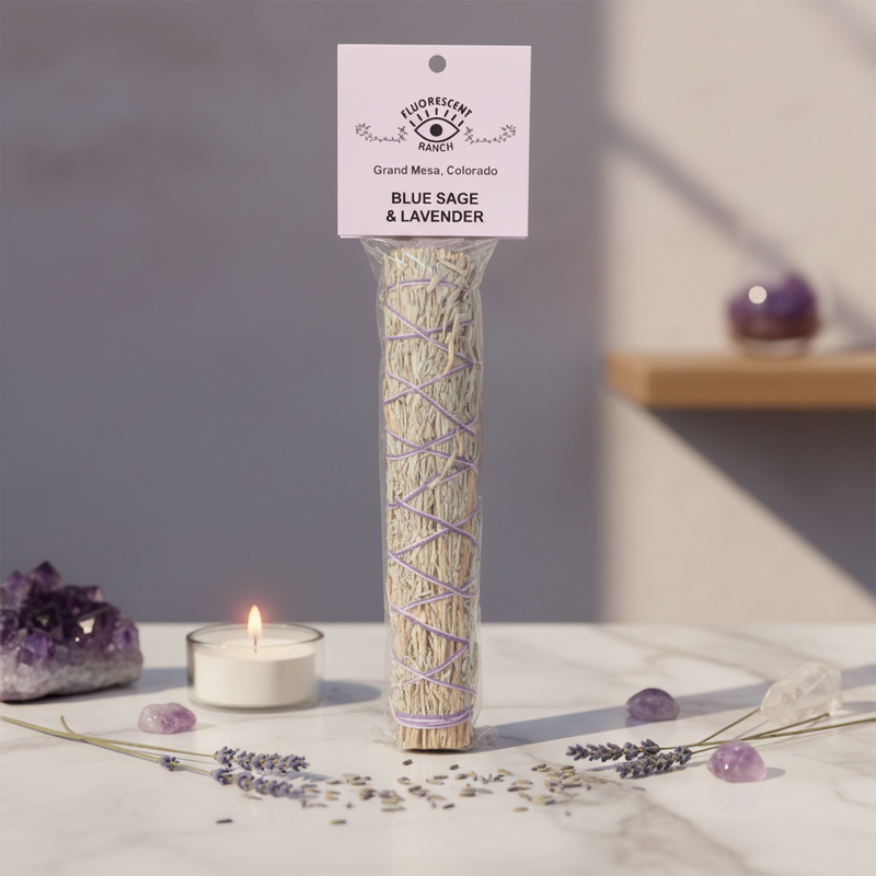 A tall clear plastic bag containing a bundle of dried blue sage and lavender smudge sticks, wrapped with purple lavender vines. The bundle has a hanging tag that reads  'BLUE SAGE & LAVENDER.