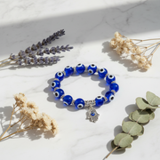 Blue beaded bracelet with a silver hamsa charm on a light surface with dried flowers.