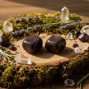 Two dark brown stones on a wooden surface with crystals and herbs