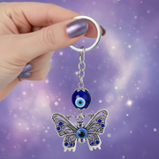 Butterfly keychain with blue evil eye charm held by a hand against a purple background