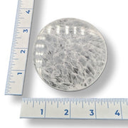 Round selenite plate with a ruler for scale on a white background