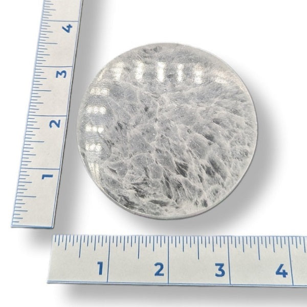 Round selenite plate with a ruler for scale on a white background