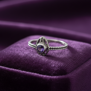 Silver ring with a purple gemstone on a purple fabric background