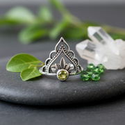 Silver ring with a green gemstone on a slate background with green beads, quartz crystal and leaves for ambiance,