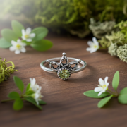 Silver ring with a green gemstone on a table surrounded by greenery and flowers.