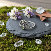 Silver ring with a green gemstone on a slate disk with flowers and crystals.