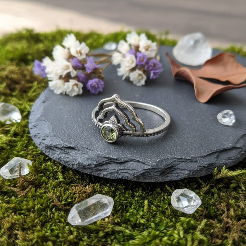 Silver ring with a green gemstone on a slate disk with flowers and crystals.