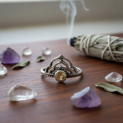 Silver ring with a yellow gemstone on a wooden surface with crystals and sage.