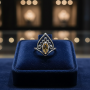 Silver ring with a yellow gemstone on a blue velvet cushion against a blurred background