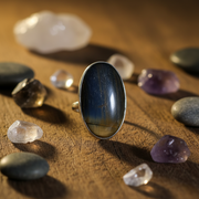 Silver ring with a dark stone on a wooden surface with various crystals