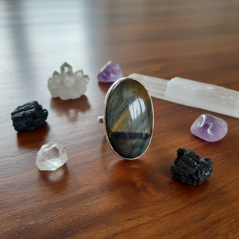 Silver ring with a large stone on a wooden surface with crystals and tools.