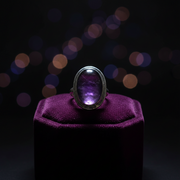 Ring with a purple gemstone on a purple cushion against a dark background with bokeh lights