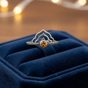 Silver ring with a central orange stone on a blue ring box.