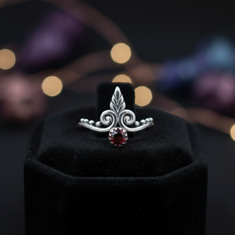 Silver ring with a red gemstone on a black stand against a blurred colorful background