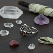 Silver ring with a red gemstone surrounded by crystals on a dark surface