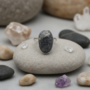 Silver ring with an oval stone on a river stone surrounded by other stones.