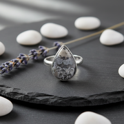 Silver ring with a teardrop-shaped stone on a slate background with herbs and white stones.
