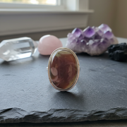 Ring with a large brown stone on a dark surface with crystals in the background
