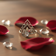 Silver ring with intricate design on a table  surrounded by stones and rose petals.
