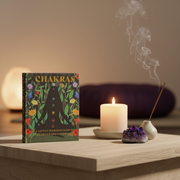 Book titled 'Chakras' on a table with a candle and incense sticks in a serene setting.