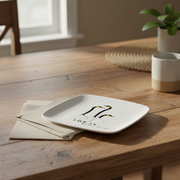 White ceramic plate with black design on a wooden table with a plant and cup in the background
