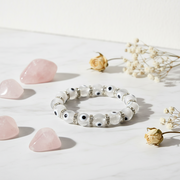 White beaded bracelet with black accents on a light surface with pink stones and dried flowers.