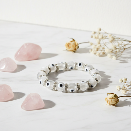 White beaded bracelet with black accents on a light surface with pink stones and dried flowers.