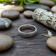 Silver ring with intricate design on a wooden surface with stones and sage.