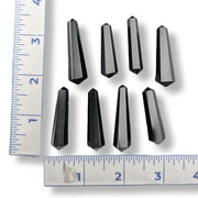Eight faceted black crystal points arranged on a white background with two metal rulers on the left and bottom edges for size reference.