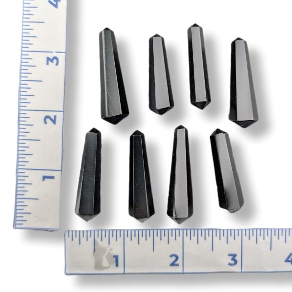 Eight faceted black crystal points arranged on a white background with two metal rulers on the left and bottom edges for size reference.