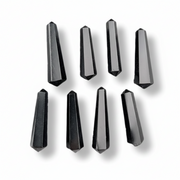 Eight faceted black crystal points arranged in two rows on a white background, each casting a soft shadow.