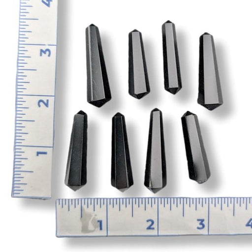 Eight faceted black crystal points arranged on a white background with two metal rulers on the left and bottom edges for size reference.