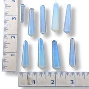 Nine small faceted blue crystal points arranged on a white background with ruler markings along the left and bottom edges for size reference.