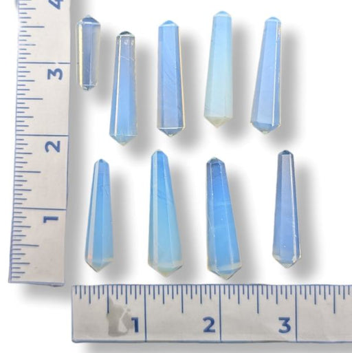 Nine small faceted blue crystal points arranged on a white background with ruler markings along the left and bottom edges for size reference.