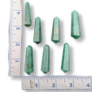 Seven green faceted crystal points arranged on a white background with ruler measurements along the left and bottom edges to show size.