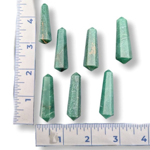 Seven green faceted crystal points arranged on a white background with ruler measurements along the left and bottom edges to show size.