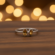 Silver ring with two yellow gemstones on a wooden surface with blurred lights in the background
