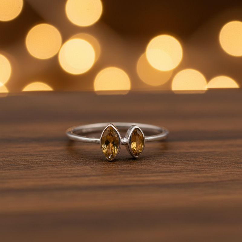 Silver ring with two yellow gemstones on a wooden surface with blurred lights in the background