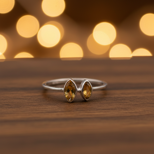 Silver ring with two yellow gemstones on a wooden surface with blurred lights in the background