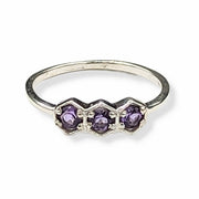 Silver ring with three purple gemstones on a white background