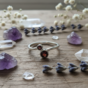 Silver ring with red gemstones on a wooden surface with crystals and flowers