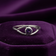 Silver ring with a purple gemstone on a purple fabric background