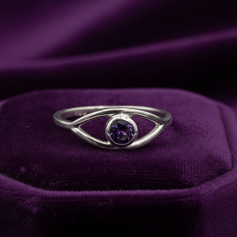 Silver ring with a purple gemstone on a purple fabric background
