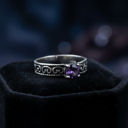 Silver ring with a purple gemstone on a black velvet stand with a dark background
