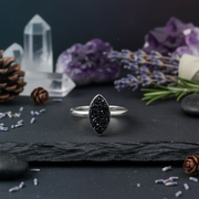 Silver ring with black gemstone on a dark surface with crystals and flowers