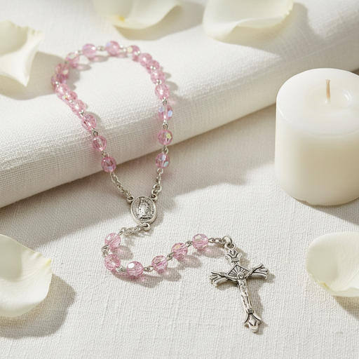 Pink beaded rosary with silver cross on a white fabric background
