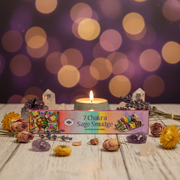 a box of 7 chakra smudge incense on a wooden white table with flower dotted around and a tea light candle and crystals