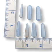 Seven small pale blue pointed crystal or gemstone pieces arranged on a white background with ruler markings visible to show size.