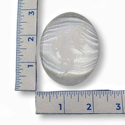 Selenite palm stone  with a etched dragon next to two rulers for size comparison on a white background